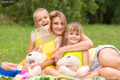 Image of Young mother on a picnic hugging two daughters, five and seven years