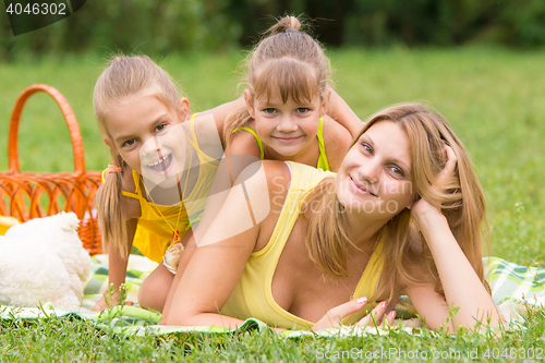 Image of Mother and two daughters lie on each other on the green grass