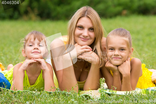 Image of Mother and two daughters lie on the green grass and propping up hands a head looked in the picture
