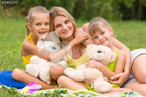 Image of Two daughter kissing and hugging her mother lying on the grass on a picnic