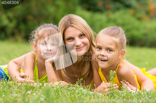 Image of Mother and two daughters lie on the green grass, and looked into the frame