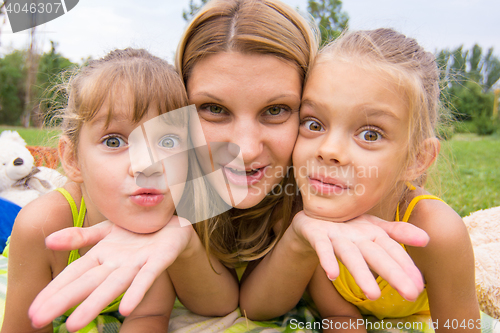 Image of Two girls resting her head on her mother\'s palm and fun look into the frame