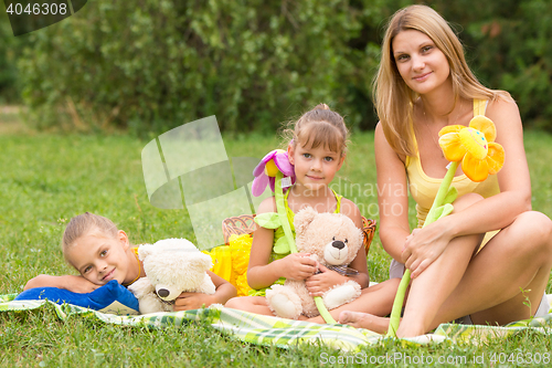 Image of Mother and daughter sitting with soft toys on a picnic and watch the shot