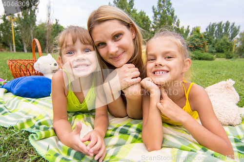 Image of Mother and two girls lying on the grass on a picnic and fun look into the frame