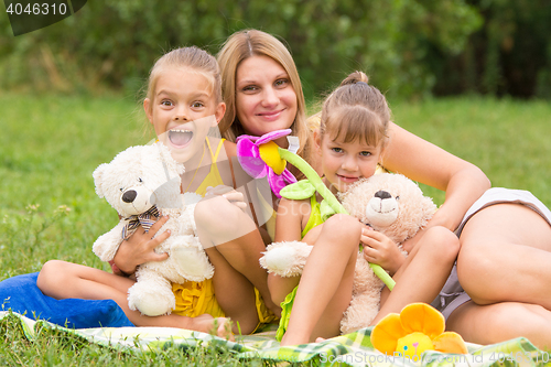 Image of Mother and two daughters sitting with soft toys on a picnic