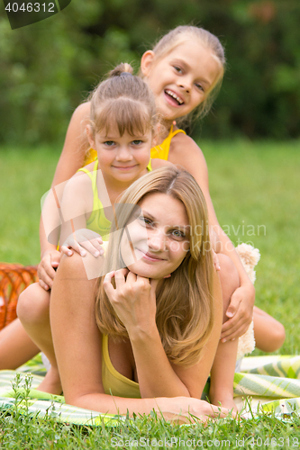 Image of Two daughters are sitting on the young mother, who is lying on the green grass