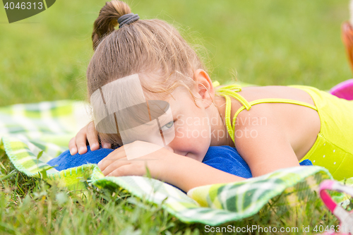 Image of Five-year girl lies on a bed on a green meadow and artfully looks aside