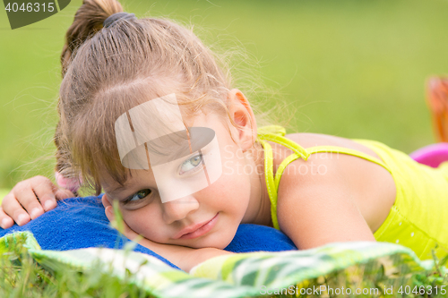 Image of Five-year girl lies on a bed on a green meadow and thoughtfully looks aside