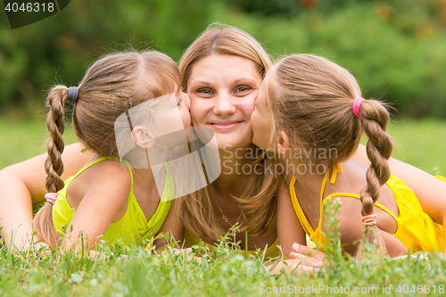 Image of Two daughters kissing mother lying on the grass on a picnic