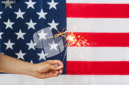 Image of close up of hand with sparkler over american flag