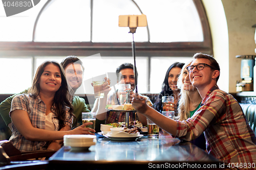 Image of happy friends with selfie stick at bar or pub