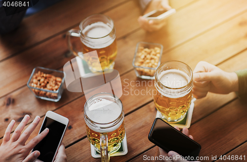 Image of close up of hands with smartphones and beer at bar