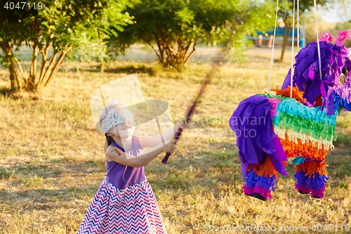 Image of Young girl at an outdoor party hitting a pinata