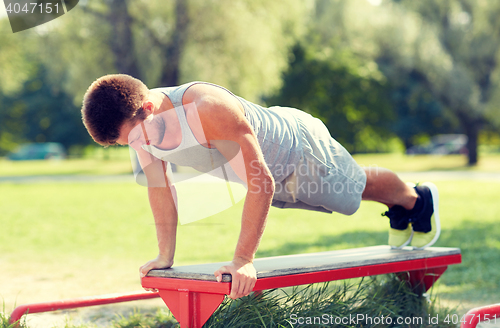 Image of young man exercising on bench at summer park