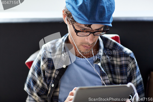 Image of man with tablet pc and earphones sitting at cafe