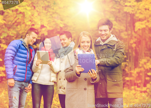 Image of group of smiling friends with tablets in park