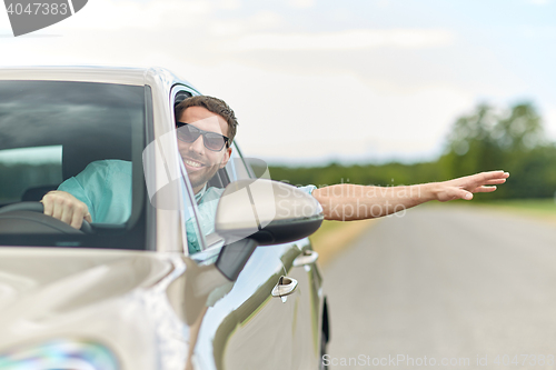 Image of happy man in shades driving car and waving hand