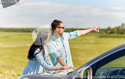 Image of man and woman with car pointing finger outdoors