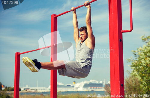 Image of young man exercising on horizontal bar outdoors