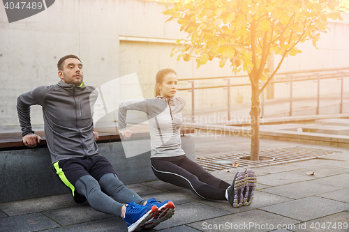 Image of couple doing triceps dip on city street bench