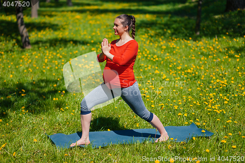 Image of Pregnant woman doing asana Virabhadrasana outdoors