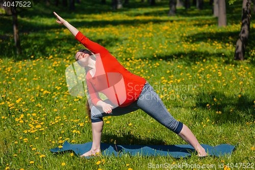 Image of Pregnant woman doing asana Utthita parsvakonasana outdoors