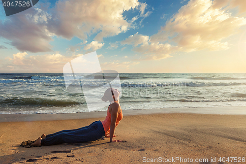 Image of Woman practices yoga asana Urdhva Mukha Svanasana at the beach