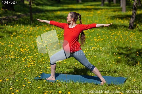 Image of Pregnant woman doing asana Virabhadrasana outdoors