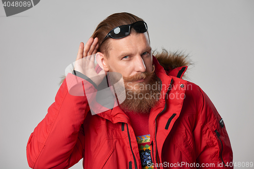 Image of Man wearing red winter jacket with hand on ear