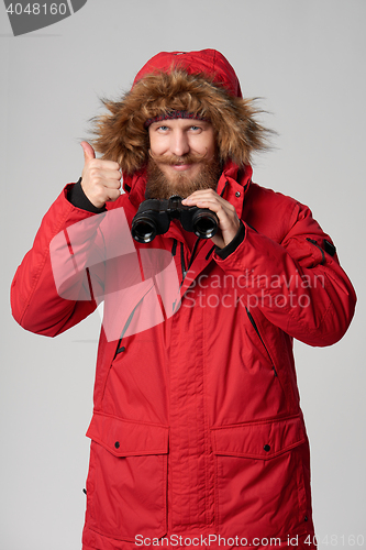 Image of Man in winter jacket holding binoculars and gesturing thumb up