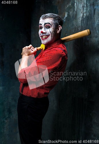 Image of The scary clown and baseball-bat on dack background. Halloween concept