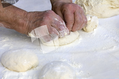 Image of Older woman hands knead dough on a table in her home kitchen