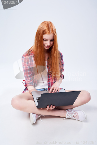 Image of Full length teen girl sitting on the floor with laptop