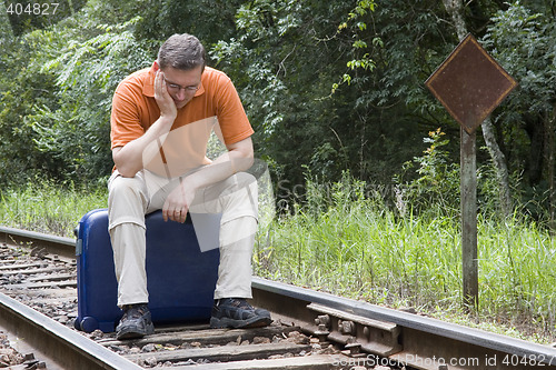 Image of Man sitting on suitcase on a railway