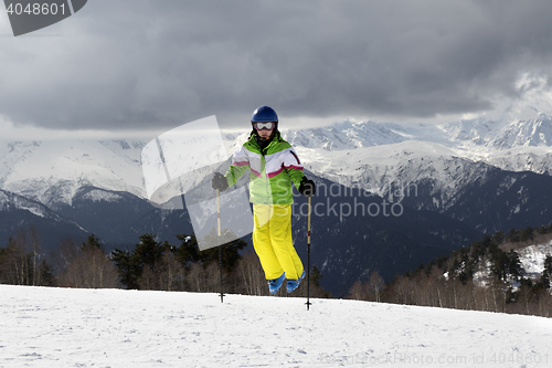 Image of Young skier jump with ski poles in sun mountains and cloudy gray