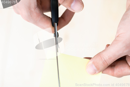 Image of A man is cutting a sheet of yellow paper using metallic scissors