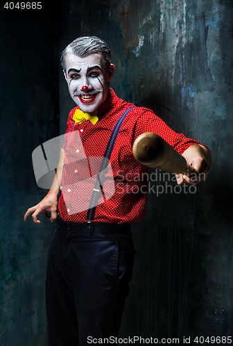 Image of The scary clown and baseball-bat on dack background. Halloween concept