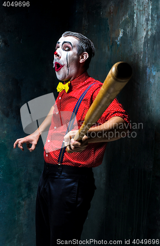 Image of The scary clown and baseball-bat on dack background. Halloween concept