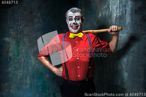 Image of The scary clown and baseball-bat on dack background. Halloween concept