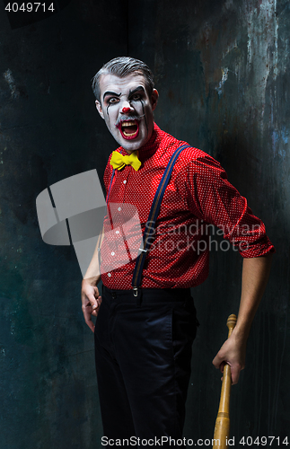 Image of The scary clown and baseball-bat on dack background. Halloween concept