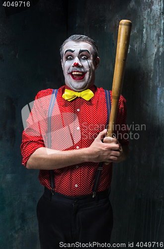 Image of The scary clown and baseball-bat on dack background. Halloween concept