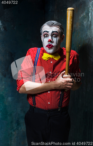 Image of The scary clown and baseball-bat on dack background. Halloween concept