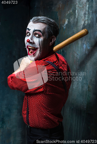 Image of The scary clown and baseball-bat on dack background. Halloween concept