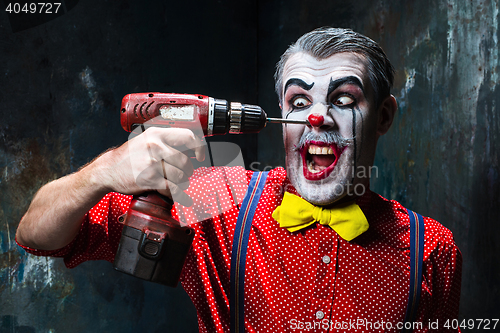 Image of The scary clown and electric drill on dack background. Halloween concept