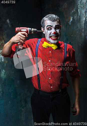 Image of The scary clown and electric drill on dack background. Halloween concept