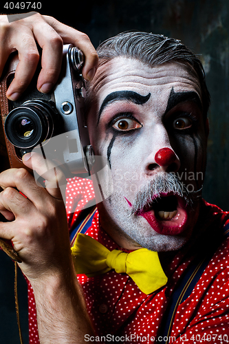 Image of The scary clown and a camera on dack background. Halloween concept