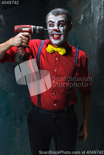 Image of The scary clown and electric drill on dack background. Halloween concept