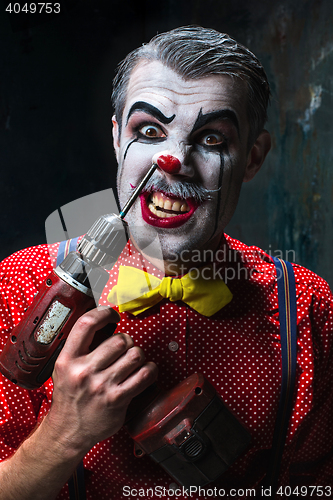 Image of The scary clown and electric drill on dack background. Halloween concept