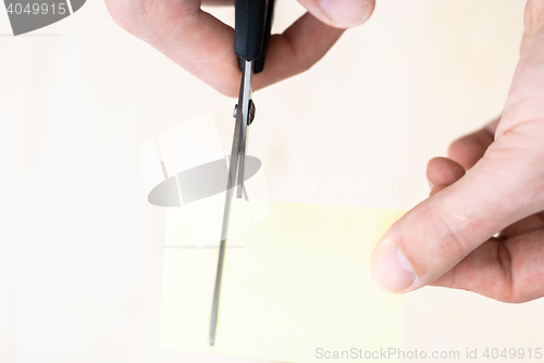 Image of A man is cutting a sheet of yellow paper using metallic scissors