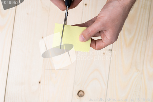 Image of A man is cutting a sheet of yellow paper using metallic scissors